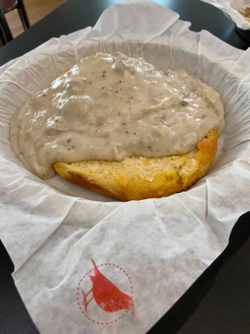 A biscuit topped with creamy sausage gravy, served on a paper-lined plate.
