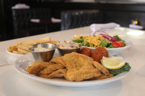 A plate of fried fish with lemon, coleslaw, and hushpuppies, accompanied by a side salad and fries.