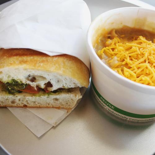 A sandwich with pesto, tomatoes, and cheese next to a cup of chili topped with shredded cheese.