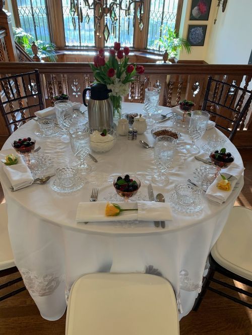 A beautifully set dining table with crystal glassware, fruit desserts, and a floral centerpiece in an elegant room.
