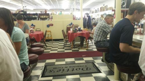 A cozy diner interior with red tablecloths, checkered floors, and patrons seated at tables and counters.