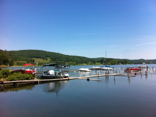 A serene lake scene with boats docked along wooden piers, surrounded by green hills under a clear blue sky.