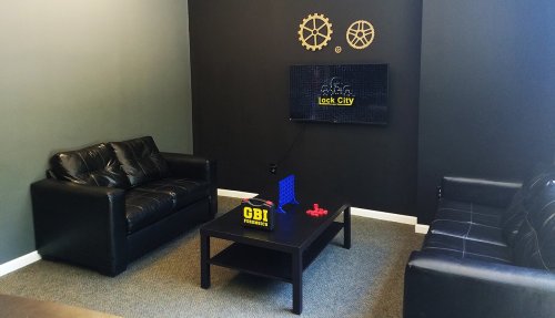 A cozy room with two black sofas, a coffee table, and a TV displaying "Lock City" on a dark wall.