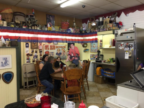 A cozy diner interior with a wooden table, chairs, and colorful decor, featuring a mural and various memorabilia on the walls.