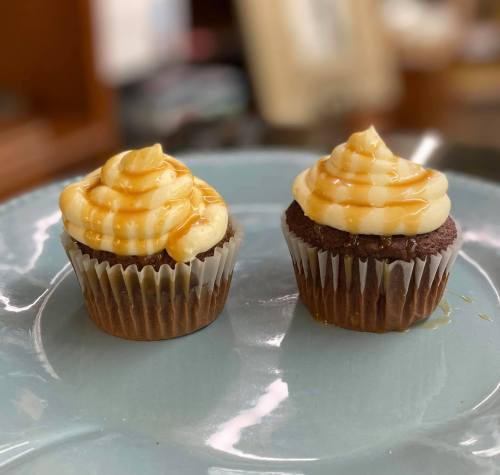 Two chocolate cupcakes with swirled vanilla frosting and drizzled caramel, placed on a light blue plate.