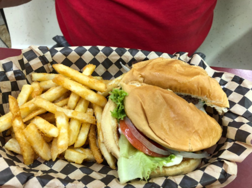 A burger with lettuce, tomato, and mayo, served with a side of golden fries in a checkered basket.