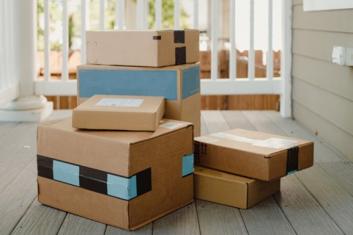 A stack of various cardboard boxes on a porch, some with blue tape and shipping labels visible.