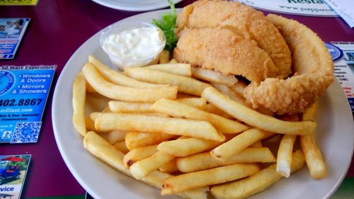 A plate of golden fried fish fillets served with a side of crispy French fries and a small cup of tartar sauce.