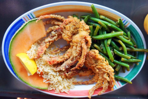 A plate of fried crab, rice, green beans, and a slice of cantaloupe, garnished with a lemon wedge.