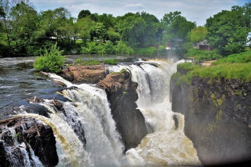 A scenic view of a waterfall cascading over rocky cliffs, surrounded by lush greenery and a river.