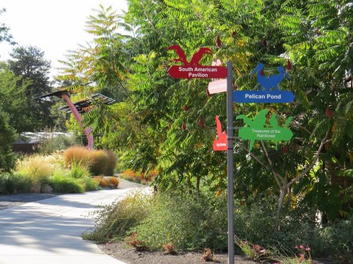 Colorful directional signs point to various attractions in a lush garden setting with greenery and pathways.