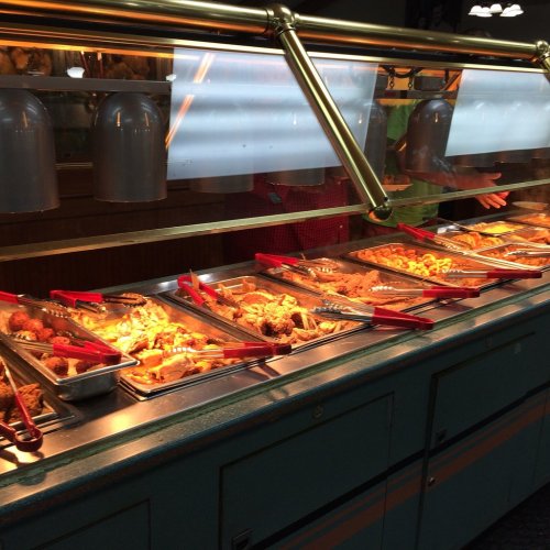 A buffet display with various dishes under warming lights, featuring trays of food and serving utensils.