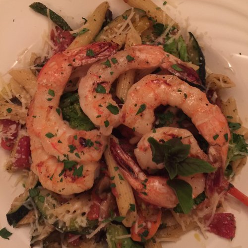 A plate of pasta with grilled shrimp, mixed vegetables, and garnished with herbs and cheese.