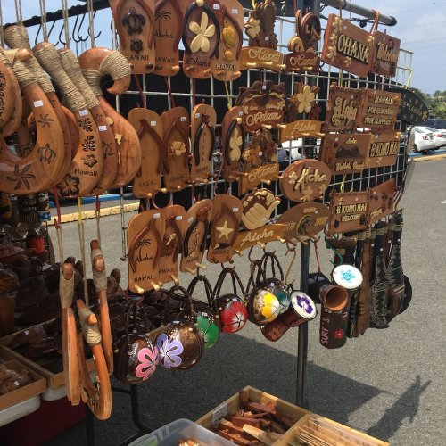 A display of wooden souvenirs and crafts, featuring Hawaiian-themed designs and carvings, at an outdoor market.