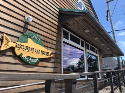 Sign for Ecola Restaurant and Market, featuring a fish design, on a wooden building with large windows.