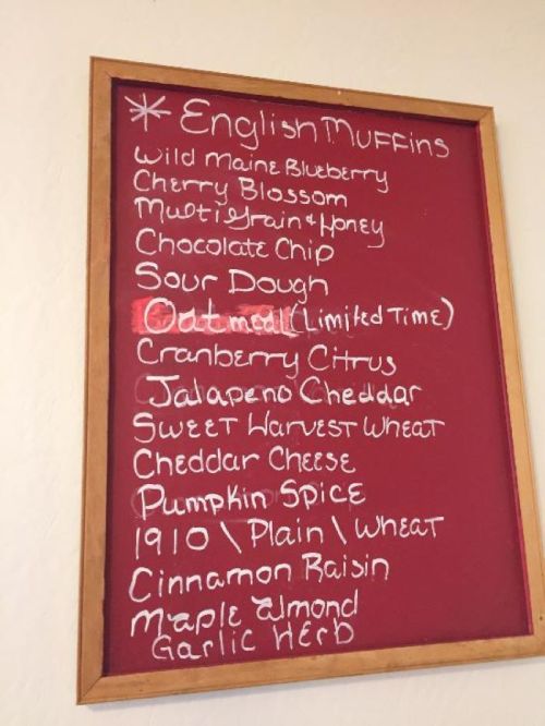 A chalkboard menu listing various flavors of English muffins, including blueberry, chocolate chip, and pumpkin spice.