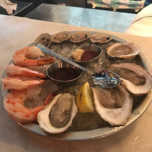 A seafood platter featuring shrimp and oysters on ice, served with lemon and dipping sauces in small bowls.