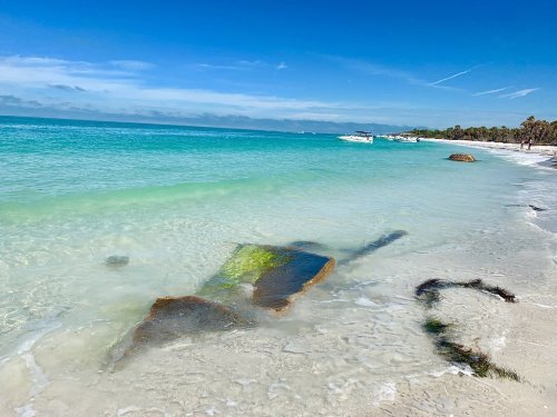 A serene beach scene with clear turquoise water, gentle waves, and rocks partially submerged in the sand.