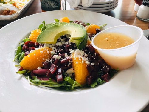 A colorful salad with arugula, beets, orange segments, avocado, feta cheese, and a side of dressing.