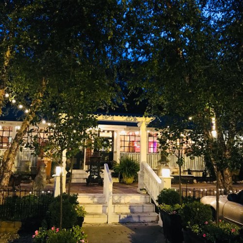 A charming restaurant entrance at night, surrounded by trees and string lights, with a welcoming atmosphere.