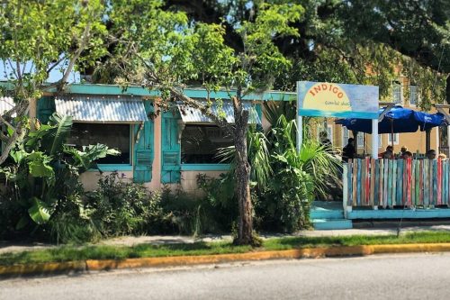 A colorful restaurant named "Indigo" with outdoor seating, surrounded by greenery and trees.