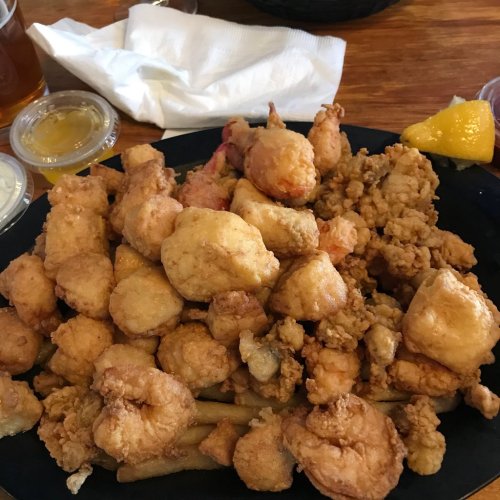 A large plate of golden fried seafood, including shrimp and fish, served with lemon and dipping sauces.