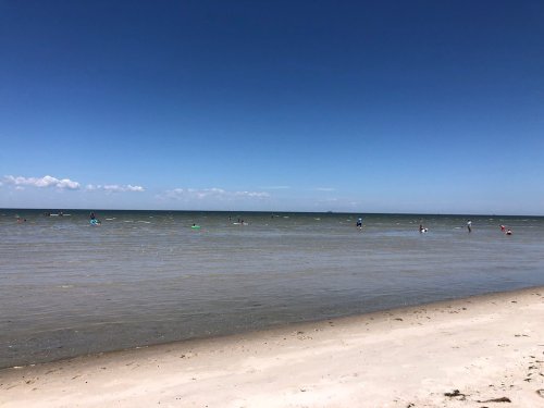 A sunny beach scene with people wading in the water and a clear blue sky above.
