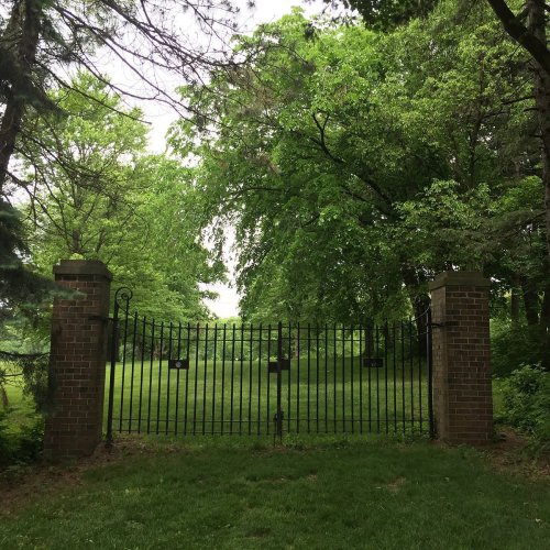 A black wrought iron gate stands open, leading into a lush green area surrounded by trees.