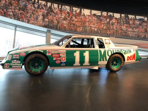 A vintage race car with a green and white Mountain Dew design, number 11, displayed in a museum setting.