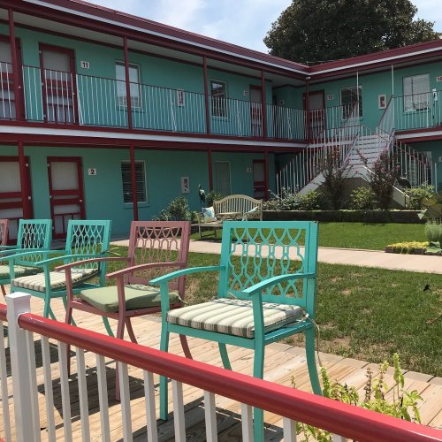 Colorful outdoor seating in front of a turquoise motel with a green lawn and stairs leading to upper floors.