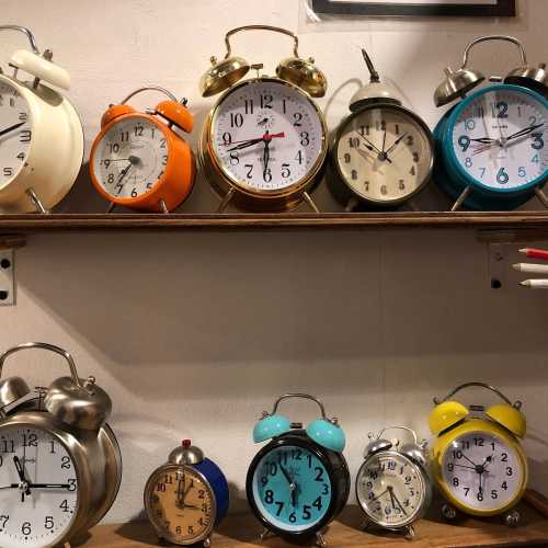 A collection of various vintage-style alarm clocks in different colors and designs displayed on a wooden shelf.