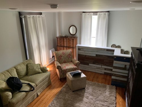 Cozy living room with a green sofa, floral armchair, wooden furniture, and large windows with white curtains.