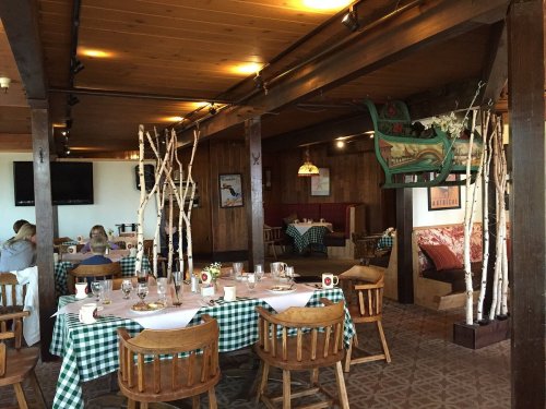 Cozy restaurant interior with wooden beams, checkered tablecloths, and rustic decor, featuring a sleigh and birch branches.