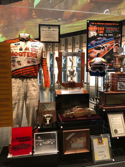 Display case featuring a racing suit, trophies, helmets, and memorabilia from the Hooters 500 event.