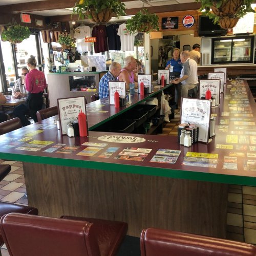 A bustling diner interior with a long counter, ketchup bottles, and patrons enjoying their meals.