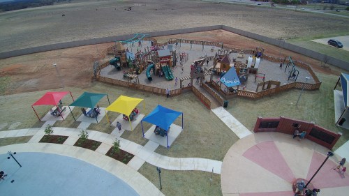 Aerial view of a playground with colorful canopies, surrounded by open fields and a walking path.