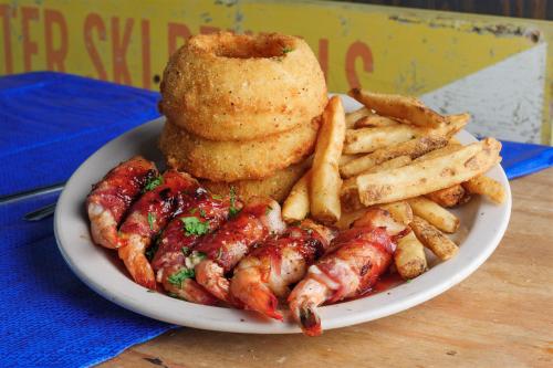 A plate of crispy onion rings, golden fries, and shrimp wrapped in bacon with a tangy sauce, garnished with herbs.