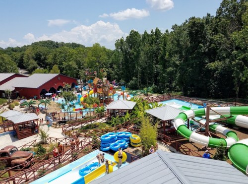 Aerial view of a vibrant water park with slides, pools, and lush greenery under a blue sky.