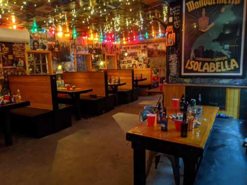 Cozy restaurant interior with colorful lights, wooden booths, and a long table with empty bottles and cups.