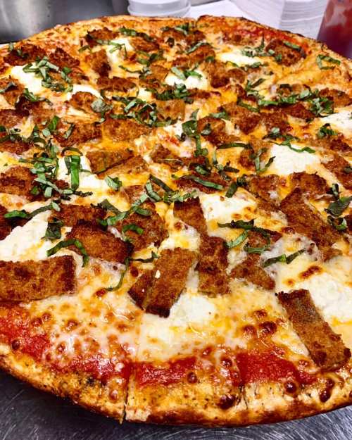 A large pizza topped with mozzarella cheese, crispy breaded pieces, and fresh basil on a golden crust.