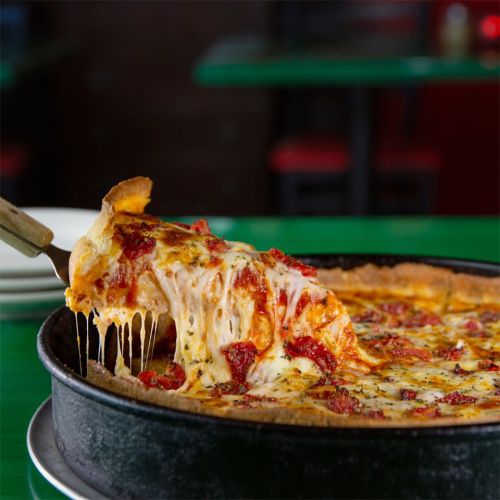 A slice of cheesy pizza being lifted from a deep dish, with gooey cheese stretching from the pie.