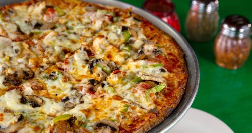A close-up of a delicious pizza topped with cheese, mushrooms, green peppers, and chicken, with condiments in the background.