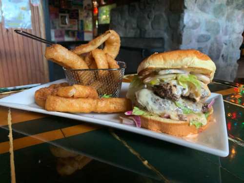 A juicy burger with lettuce, cheese, and onions, served with onion rings and fries on a plate.