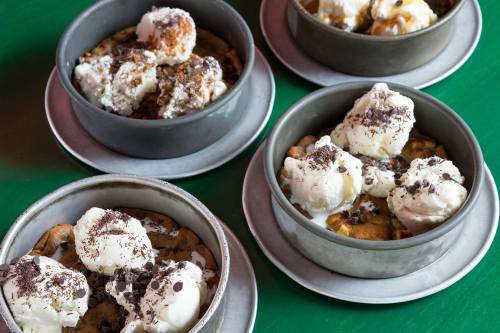 Four round metal dishes filled with warm desserts topped with scoops of ice cream and chocolate shavings.