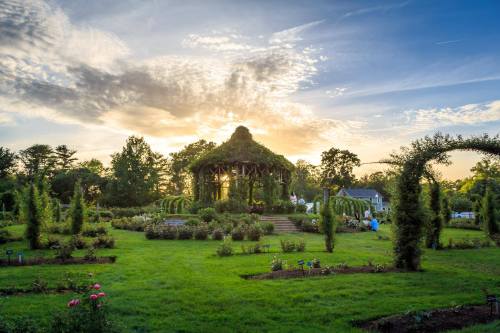 A lush garden at sunset, featuring a vine-covered gazebo and neatly arranged flower beds under a colorful sky.