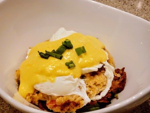 A bowl of poached eggs on a bed of savory stuffing, topped with creamy hollandaise sauce and green onion.