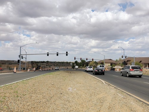 Traffic lights at an intersection with construction, surrounded by houses and a cloudy sky.