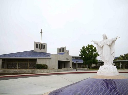 A modern church building with a blue roof and a statue of Jesus with outstretched arms in the foreground.