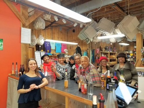 A group of seven people smiling at a bar, with bottles and a colorful backdrop in a cozy, rustic setting.