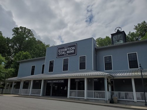 Exterior of the Exhibition Coal Mine building, featuring a sign and a porch, surrounded by trees under a cloudy sky.